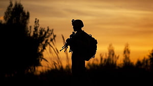 Silhouette of a soldier with rifle and backpack against a golden sunset sky HD wallpaper