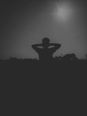 Silhouette of a person relaxing with hands behind head against a bright sun and tree line HD phone wallpaper