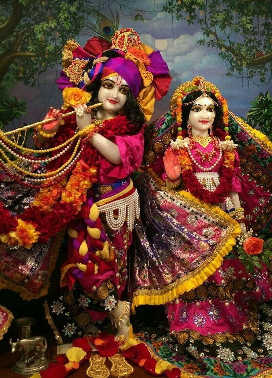 Radha Krishna idols adorned in vibrant pink and purple silk garments with floral garlands and jewelry HD phone wallpaper