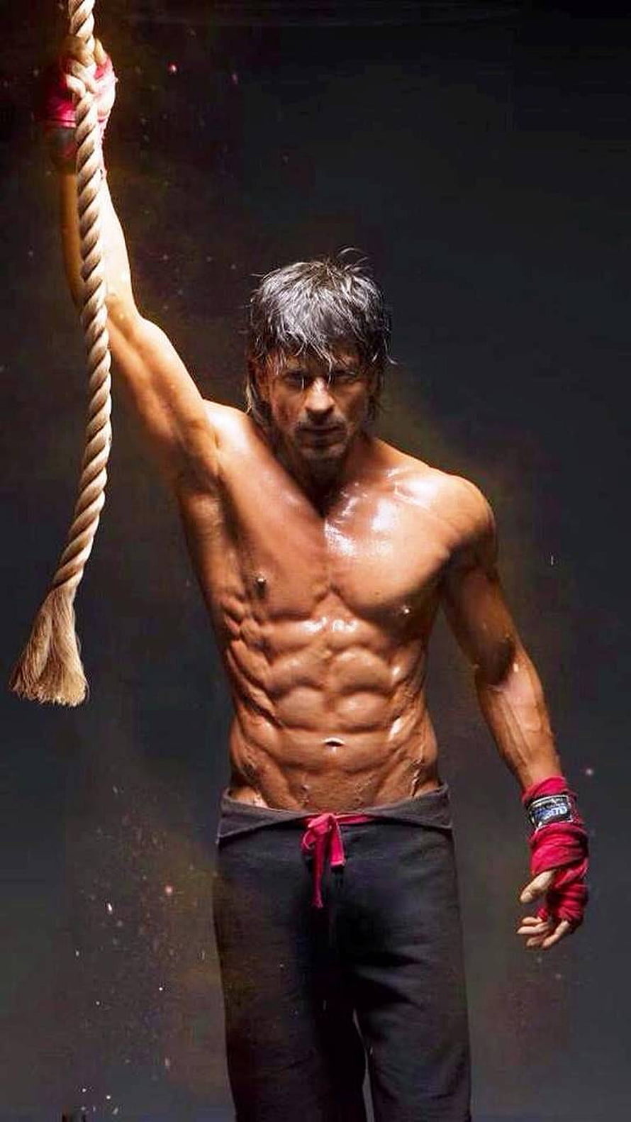 Shah Rukh Khan shirtless with defined abs gripping a rope in dramatic lighting HD phone wallpaper