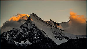 Dramatic Snow-Capped Mountain Peak at Golden Hour with Orange Clouds HD wallpaper