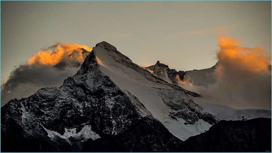 Dramatic Snow-Capped Mountain Peak at Golden Hour with Orange Clouds HD wallpaper