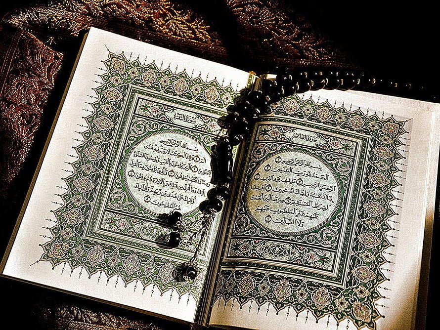Open Quran with intricate green floral borders and black prayer beads resting on ornate fabric HD wallpaper