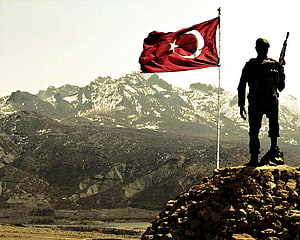 Turkish soldier silhouette standing on rocky outcrop with national flag against snow-capped mountains HD wallpaper