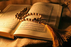 Open Quran with wooden prayer beads resting on burlap fabric in warm golden light HD wallpaper