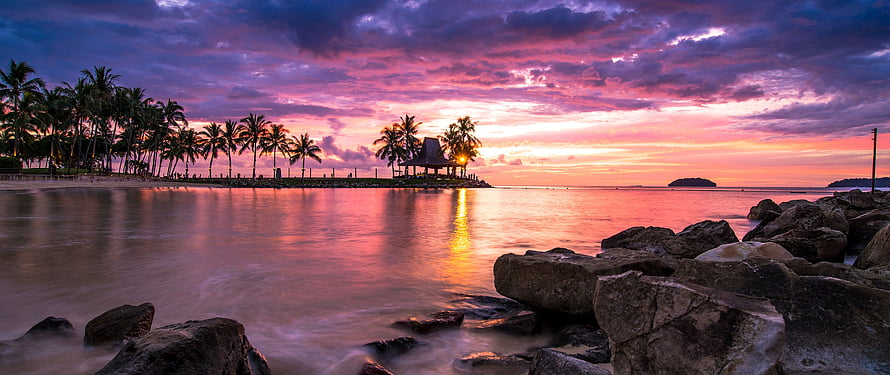 Vibrant Pink and Purple Sunset Over Tropical Beach with Palm Trees and Rocks HD wallpaper