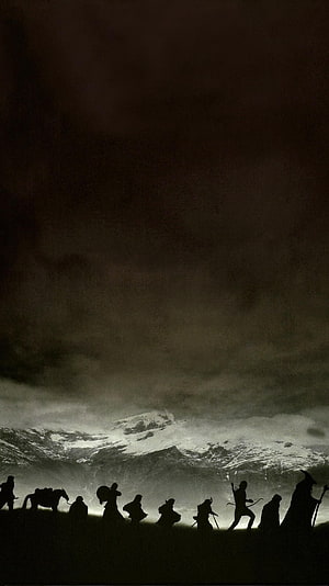 Silhouetted Fellowship of the Ring travelers crossing a dark landscape before a snow-capped mountain peak HD phone wallpaper