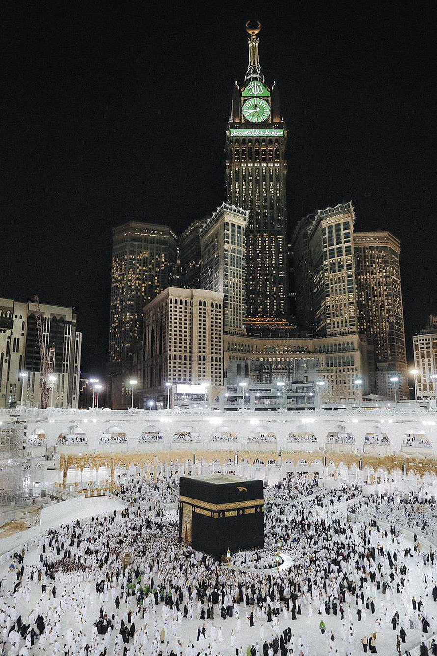 The Kaaba in Mecca at Night Surrounded by Pilgrims and the Makkah Clock Tower HD phone wallpaper