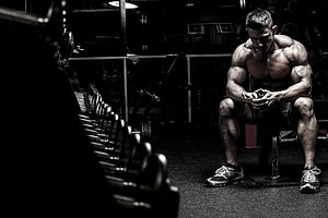 Muscular Bodybuilder Sitting on Bench in Dark Gym with Dumbbells HD wallpaper