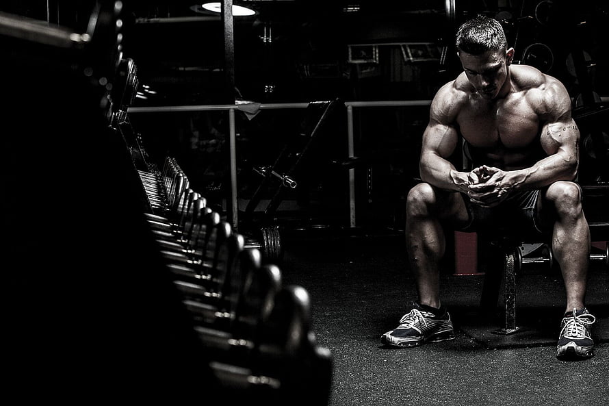 Muscular Bodybuilder Sitting on Bench in Dark Gym with Dumbbells HD wallpaper