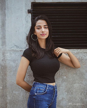Meenakshi Chaudhary in Black Top and Blue Jeans Against Concrete Wall HD phone wallpaper