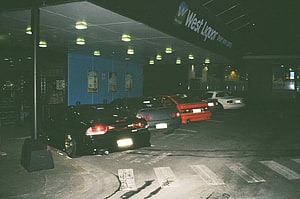 Nighttime street scene with parked cars under a liquor store awning HD wallpaper