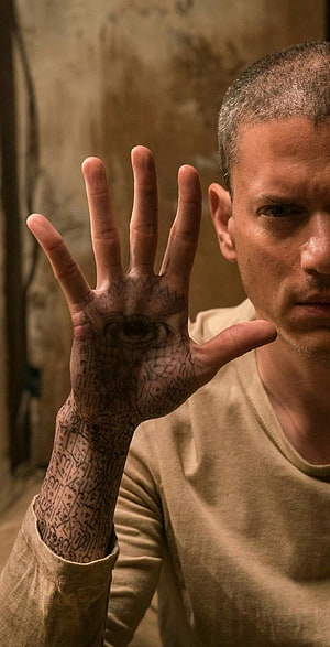 Michael Scofield with intricate hand tattoos and eye design in a dimly lit room HD phone wallpaper