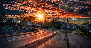 Dramatic Sunset Over a Winding Road with Fiery Orange Clouds and Suburban Buildings HD wallpaper