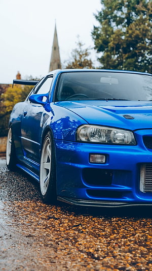 Blue Nissan Skyline GT-R R34 parked on wet autumn road with fallen leaves HD phone wallpaper