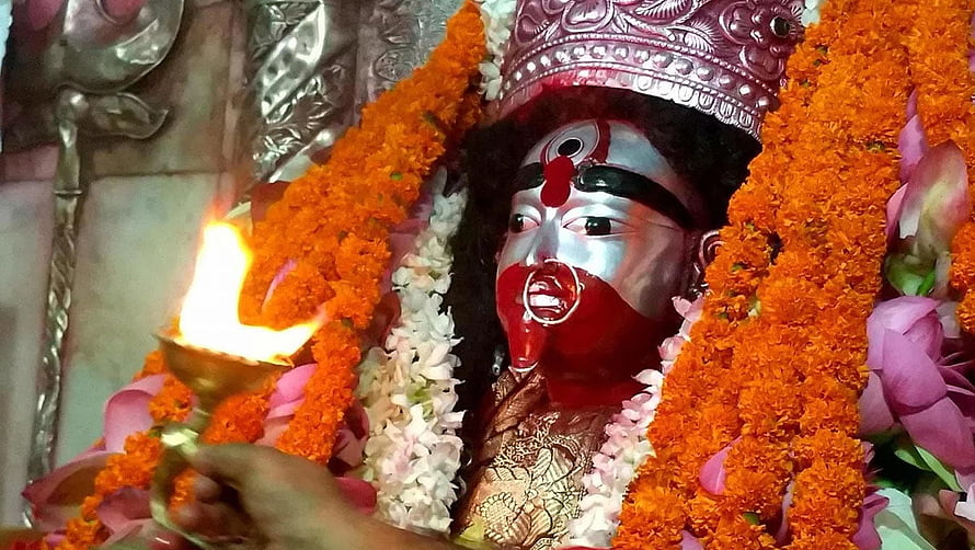 Hindu deity statue adorned with marigold garlands and silver crown during aarti ceremony with oil lamp HD wallpaper