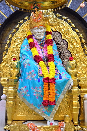 Sri Sathya Sai Baba Statue in Blue Robes and Flower Garlands on Golden Throne HD phone wallpaper
