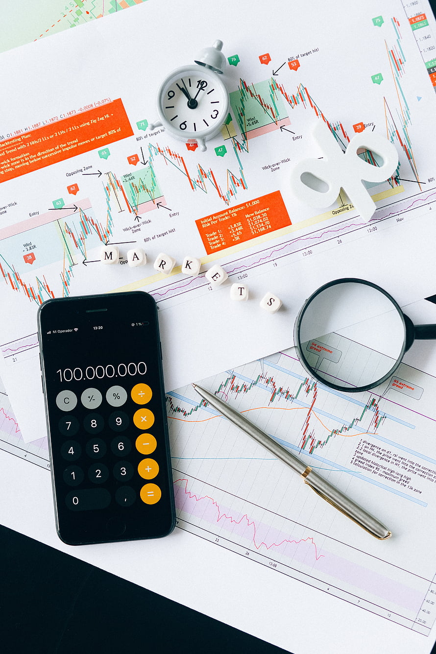 Financial trading setup with stock market charts, calculator showing profit, magnifying glass, and pen on desk HD phone wallpaper