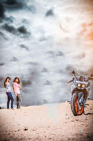 Two women standing on a sandy beach next to a parked motorcycle under a dramatic cloudy sky HD phone wallpaper