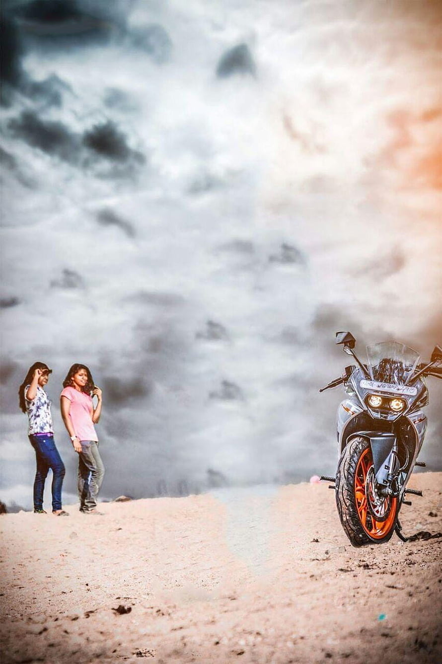 Two women standing on a sandy beach next to a parked motorcycle under a dramatic cloudy sky HD phone wallpaper