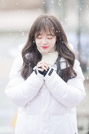 Kim Sejeong in a white winter coat and cream scarf with hands clasped in falling snow HD phone wallpaper