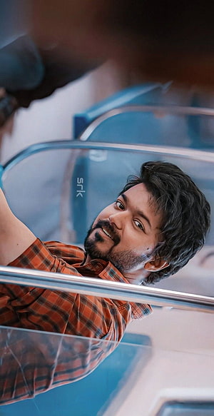 Vijay in a casual orange plaid shirt leaning on a glass railing with a warm smile HD phone wallpaper