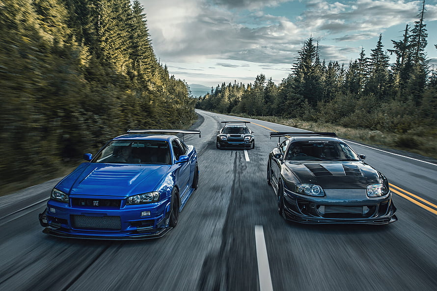 Three modified Nissan Skyline GT-Rs driving on a winding forest road HD wallpaper