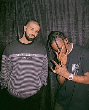 Drake and Travis Scott posing together in casual streetwear against a dark curtain backdrop HD phone wallpaper