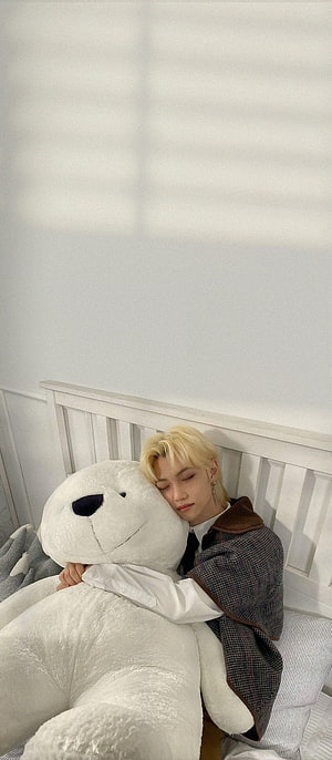 Felix from Stray Kids resting peacefully with a giant white teddy bear on a bed HD phone wallpaper