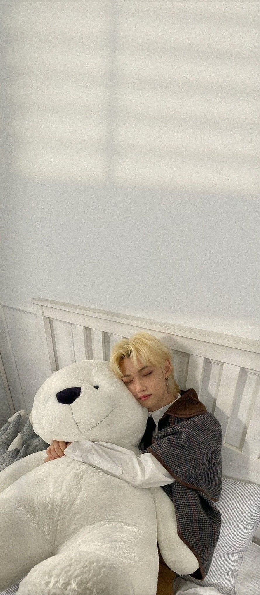 Felix from Stray Kids resting peacefully with a giant white teddy bear on a bed HD phone wallpaper