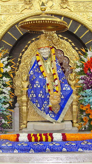 Sri Sathya Sai Baba statue seated on golden throne adorned with blue silk and flower garlands HD phone wallpaper