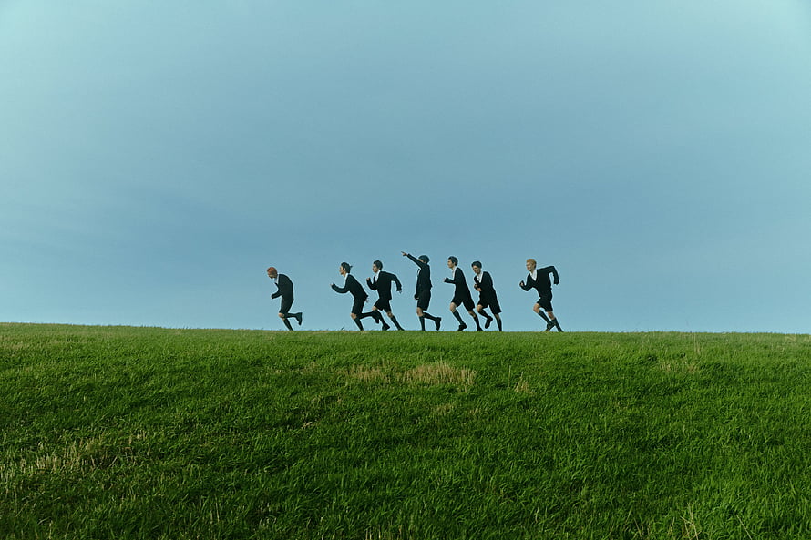 Enhypen members running across a green grassy hill under a clear blue sky HD wallpaper