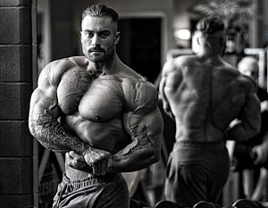 Black and white portrait of a muscular bodybuilder posing in a gym with tattoos HD wallpaper