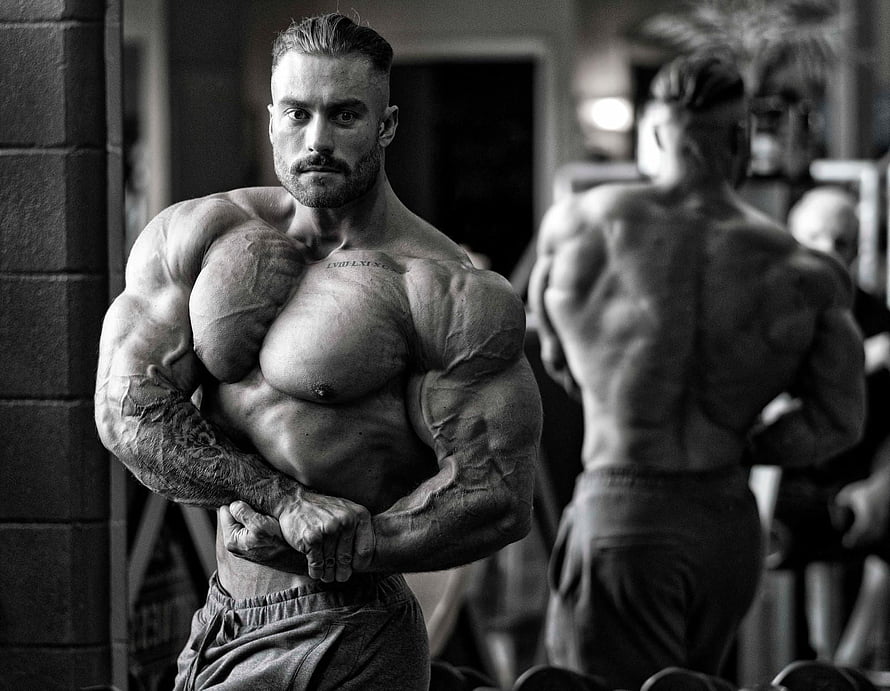 Black and white portrait of a muscular bodybuilder posing in a gym with tattoos HD wallpaper