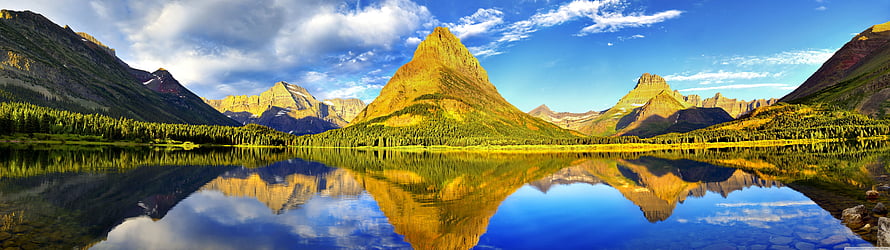 Stunning panoramic view of the Three Sisters mountains reflecting in a calm alpine lake under a blue sky with clouds HD wallpaper