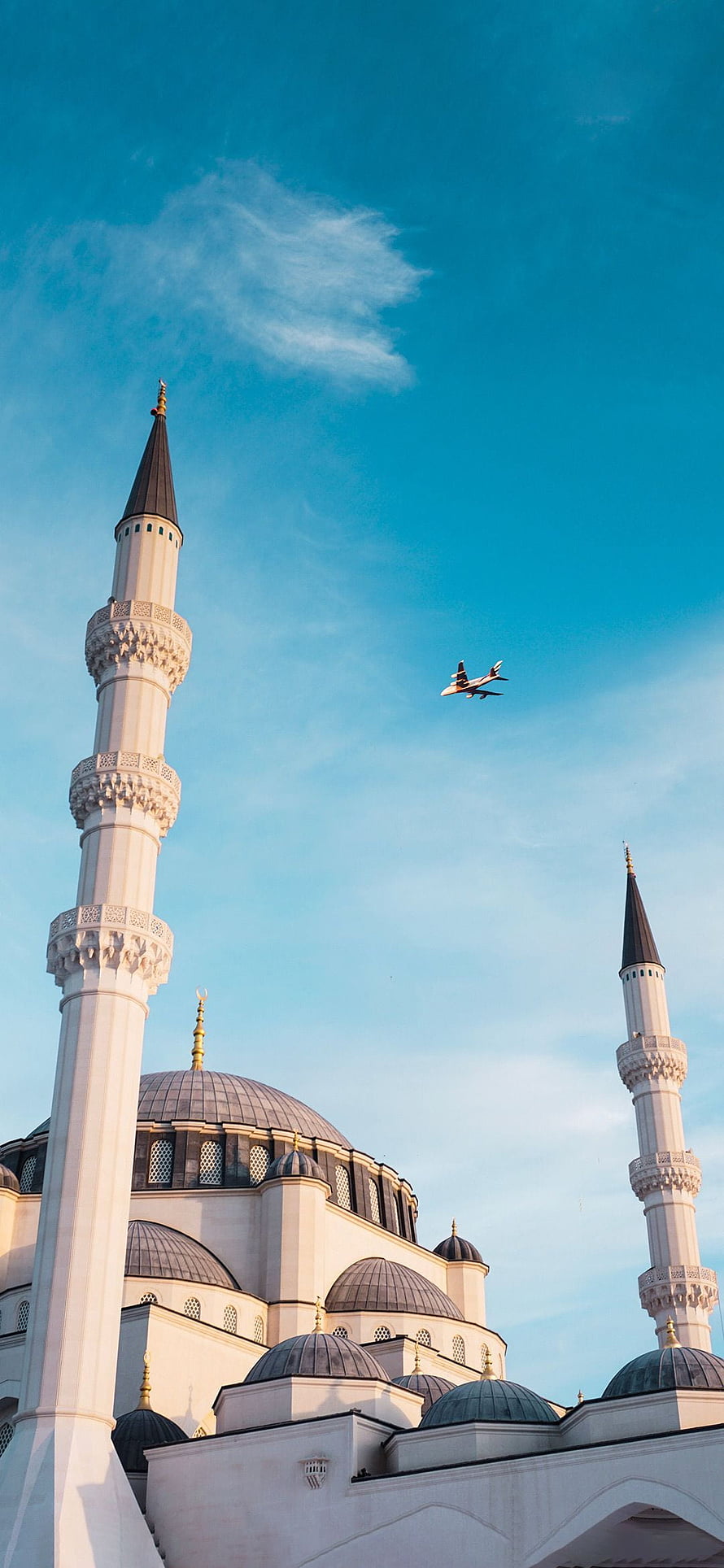 Airplane flying over mosque minarets and domes against blue sky HD phone wallpaper