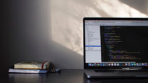 MacBook Pro on a desk displaying code editor with books and soft natural light HD wallpaper