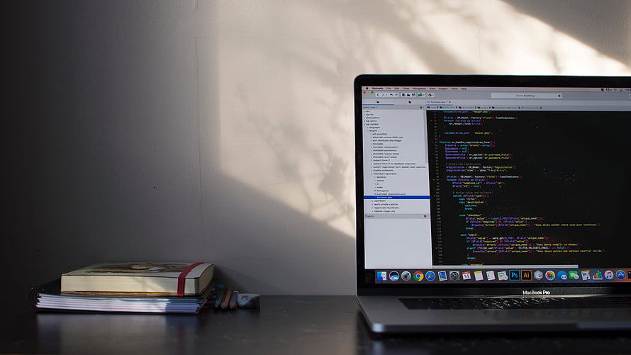 MacBook Pro on a desk displaying code editor with books and soft natural light HD wallpaper