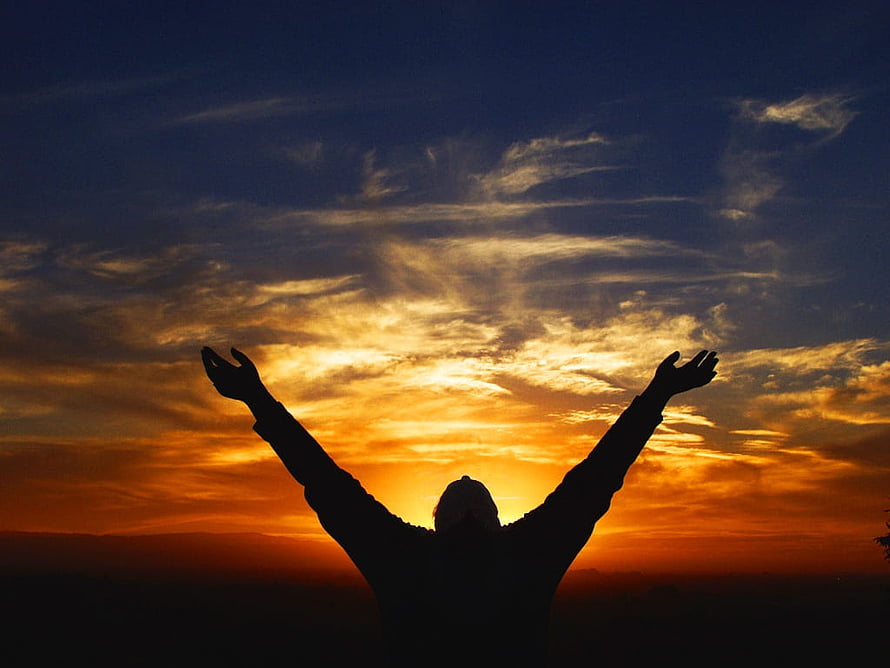 Silhouette of a person with raised arms against a vibrant sunset sky HD wallpaper