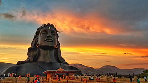 Isha Foundation Shiva Statue at Sunset with Dramatic Orange Sky and Mountain Silhouettes HD wallpaper