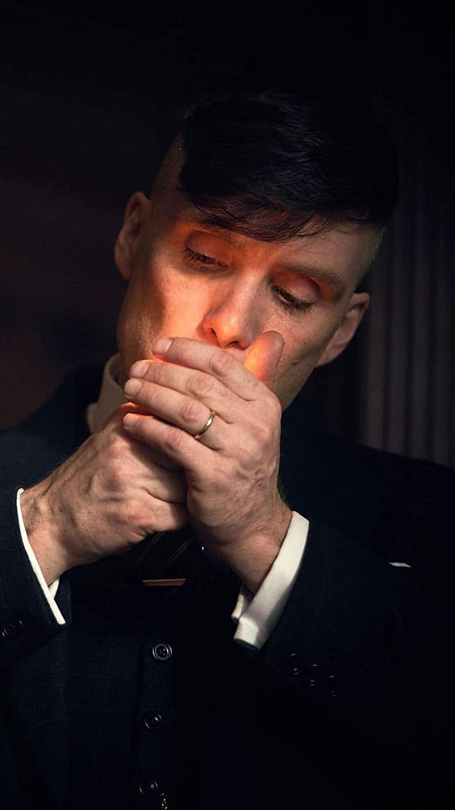 Tommy Shelby in a dark suit with hands clasped near his face in dramatic warm lighting HD phone wallpaper