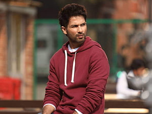 Shahid Kapoor in a maroon hoodie with a serious expression against a blurred urban background HD wallpaper