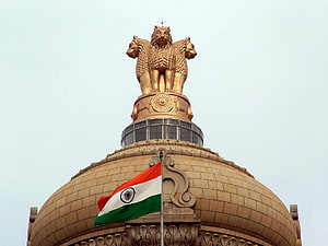 Golden Lion Capital of Ashoka atop the Indian Parliament House dome with the national flag waving against a clear sky HD wallpaper