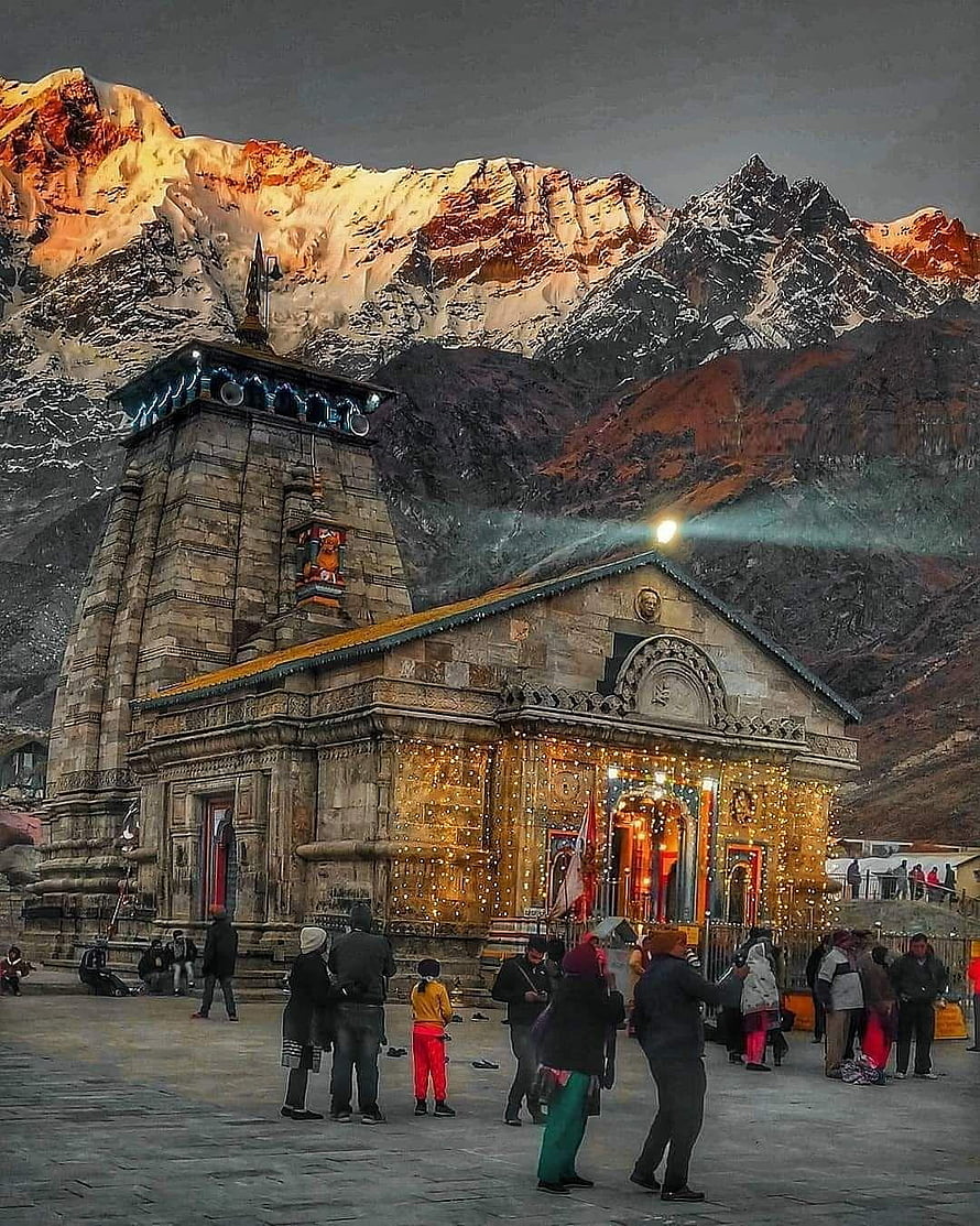 Ancient Kedarnath Temple illuminated with lights against snow-capped Himalayan mountains at sunset HD phone wallpaper