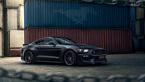 Black Ford Mustang GT parked in front of stacked shipping containers in an industrial yard HD wallpaper