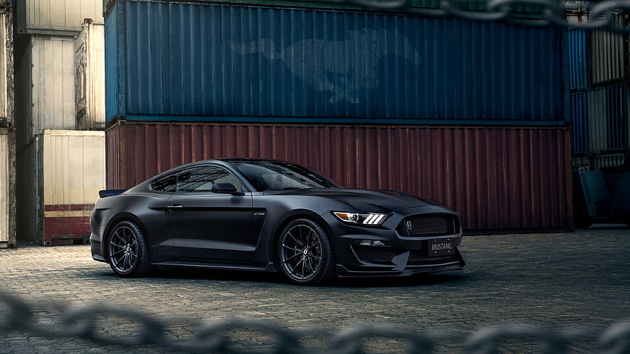 Black Ford Mustang GT parked in front of stacked shipping containers in an industrial yard HD wallpaper