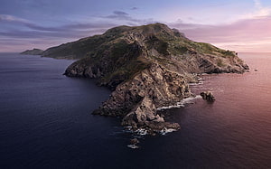 Aerial View of Rugged Coastal Island at Dusk with Dramatic Rocky Cliffs and Calm Ocean Waters HD wallpaper