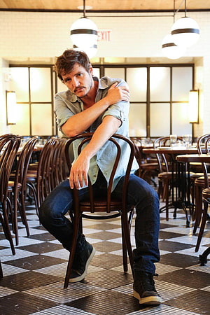 Pedro Pascal seated in a vintage cafe with checkered floor and wooden chairs HD phone wallpaper