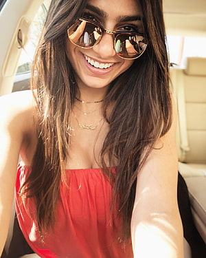 Mia Khalifa smiling in a red top and gold sunglasses inside a car HD phone wallpaper