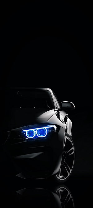 BMW M4 with glowing blue angel eye headlights in dark studio setting HD phone wallpaper